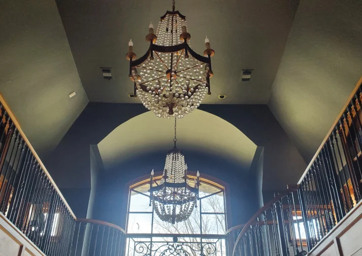 two chandeliers hanging from a tall ceiling, installed by tom king electric